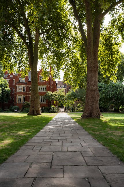 A small, well-maintained front garden in Russell Square featuring a paved pathway leading to a decorative metal garden bench positioned against a white exterior wall of a building. The garden is borde